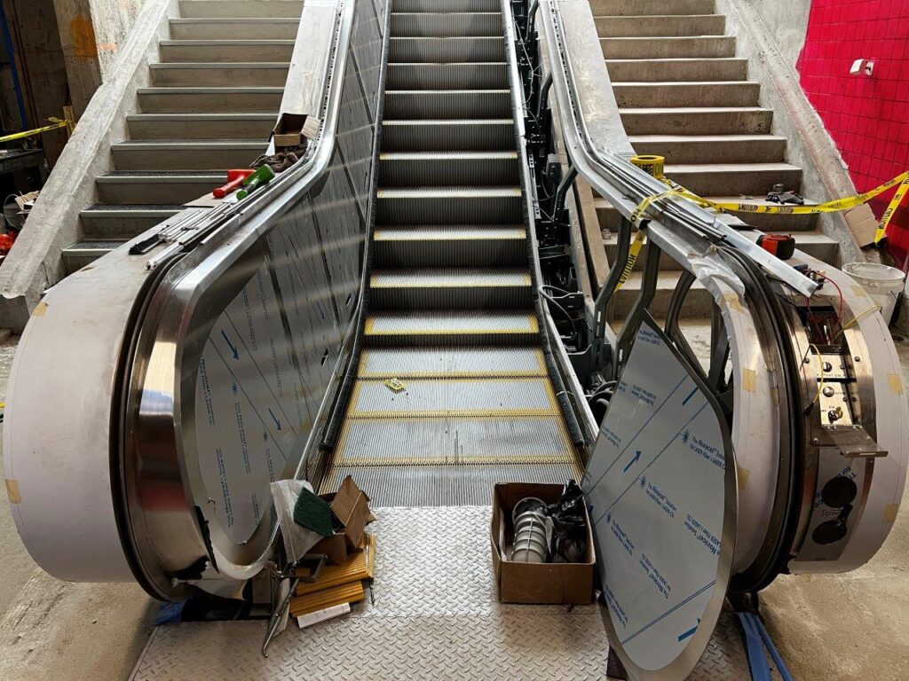 Stainless steel cladding is being installed along the sides of the escalator.